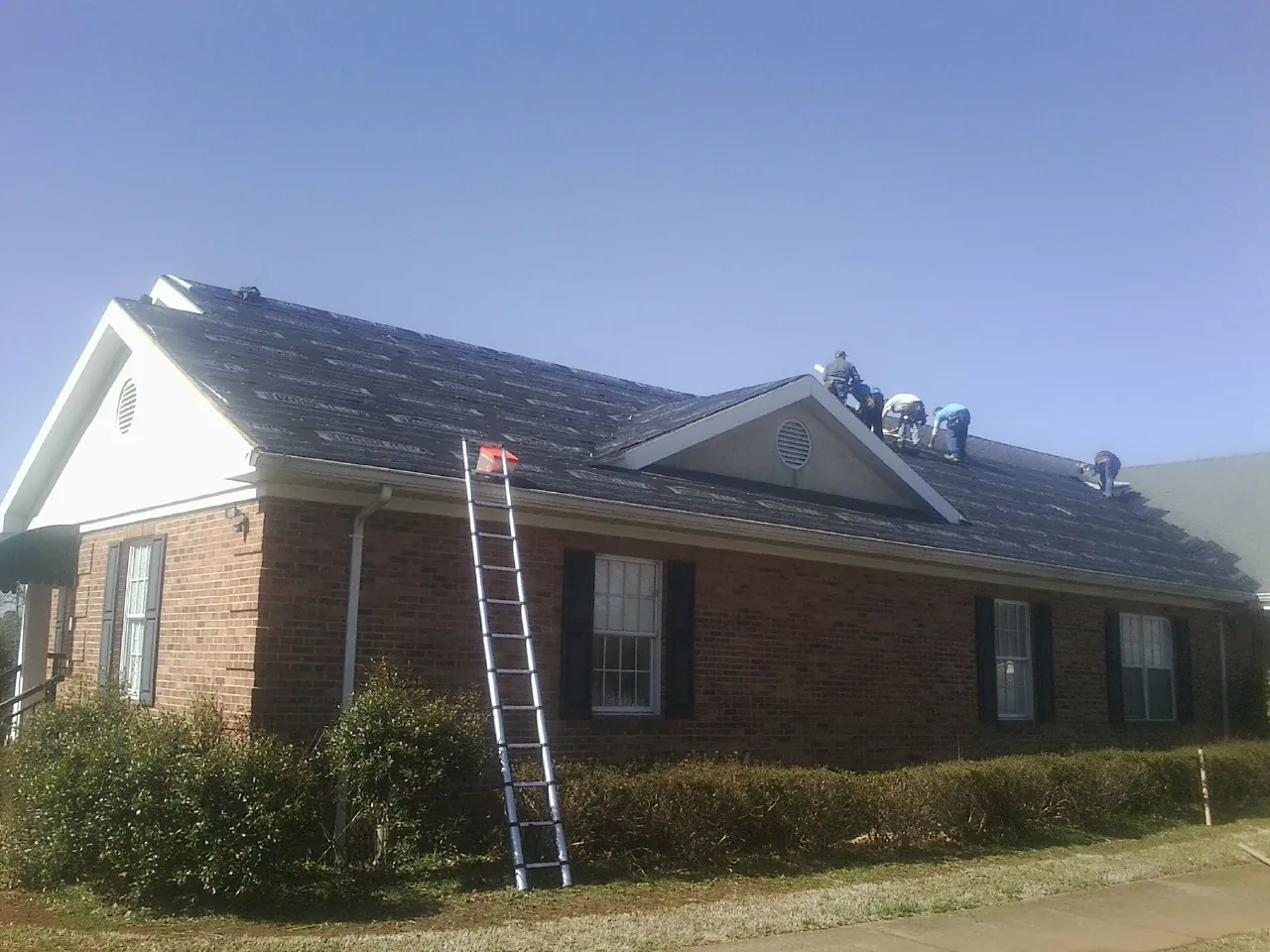 Crew tearing shingles off a brick ranch roof with a ladder set — Emergency Roof Repair work by our crew in Winamac