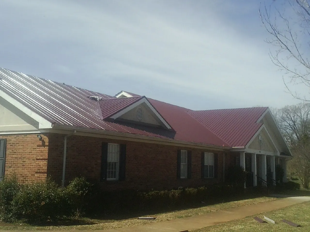 Red metal roof with gabled entries on a long brick building, from a Hail Damage Roof Repair job in Winamac
