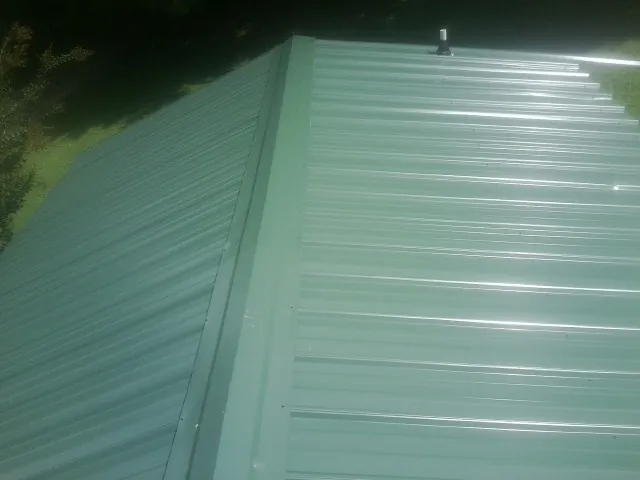 New green metal panels meeting at the ridge of a roof — Flat Roof Repair work by our crew in Winamac
