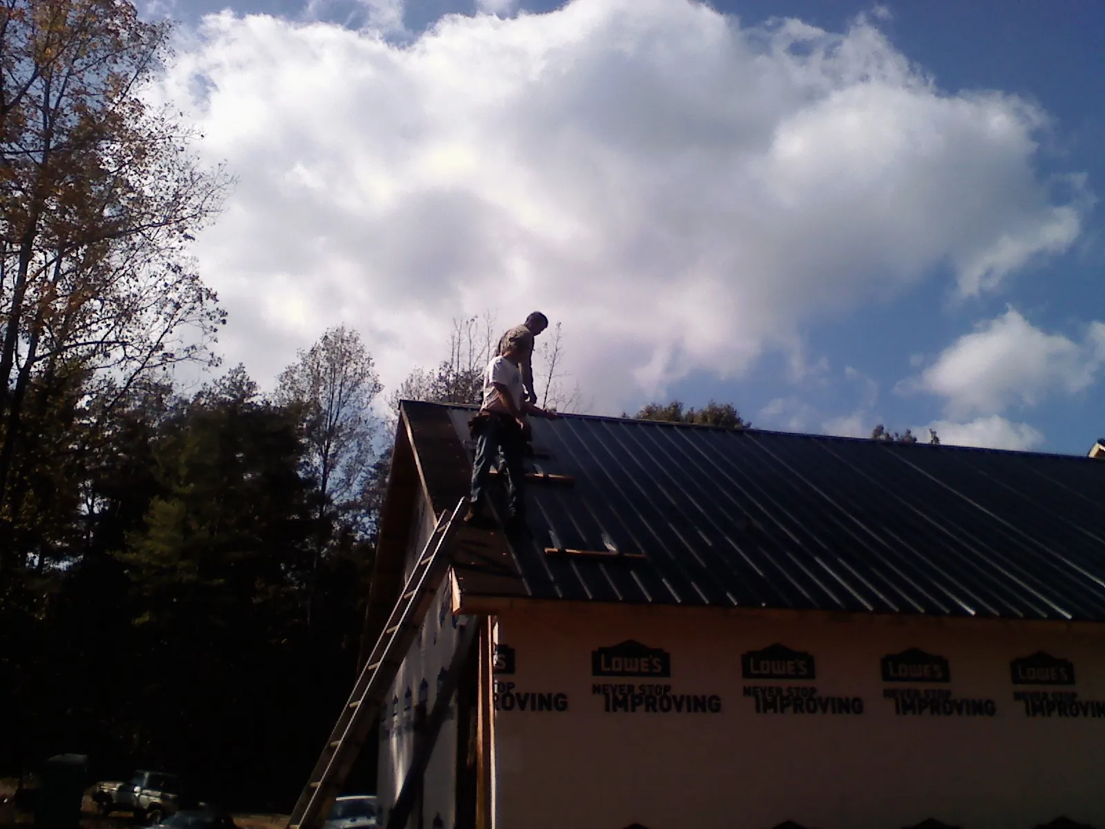 Roofer fastening dark metal panels high against a cloudy sky, from a Roof Inspection job in Winamac