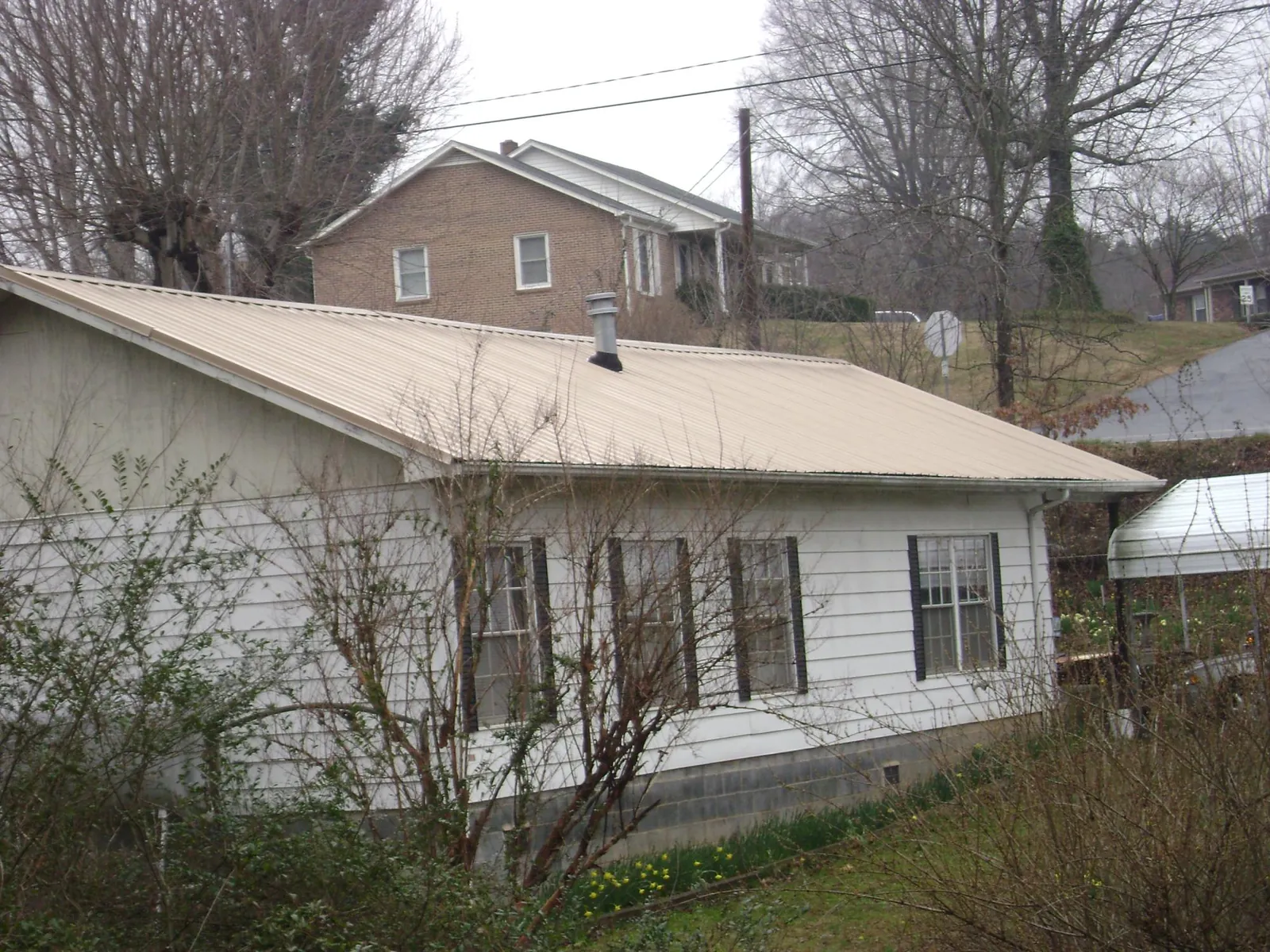 Tan metal roof on a white sided house set into a hillside — Commercial Roofing by Roofing Brothers in Winamac
